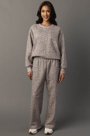 A woman stands smiling against a plain gray background, wearing the Panache Apparel Collection Cream & Brown Leopard Sweatshirt paired with matching pants and white sneakers.