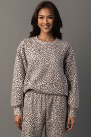 A woman smiles while wearing the Panache Apparel Collection Cream & Brown Leopard Sweatshirt with matching pants, standing against a plain gray background.