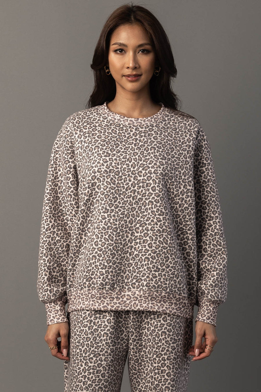 A woman wears the Panache Apparel Collection Cream & Brown Leopard Sweatshirt paired with matching pants, standing against a plain gray background and facing forward with a neutral expression.