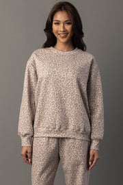 A woman smiles as she stands against a gray background, wearing the Panache Apparel Collection Blush & Light Brown Leopard Sweatshirt with long sleeves and a relaxed fit.