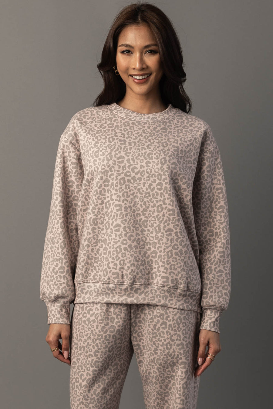 A woman smiles as she stands against a gray background, wearing the Panache Apparel Collection Blush & Light Brown Leopard Sweatshirt with long sleeves and a relaxed fit.