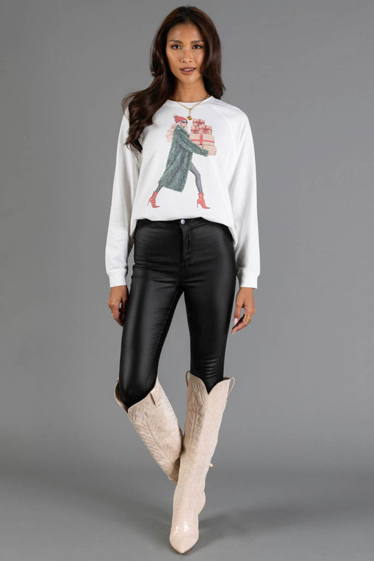 A woman wearing a Girl Carrying Christmas Presents Sweatshirt from the Panache Apparel Collection, black pants, and knee-high boots.