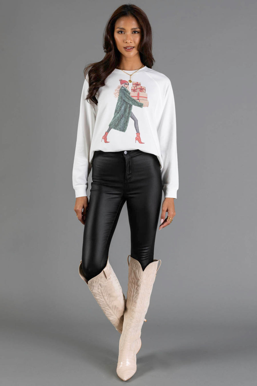 A woman wearing a Girl Carrying Christmas Presents Sweatshirt from the Panache Apparel Collection, black pants, and knee-high boots.