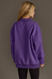 A person with long blonde hair, seen from behind, wears a loose-fitting Panache Apparel Collection Purple Game Day & Sunday Funday Reversible Sweatshirt and black pants, standing against a plain gray background.