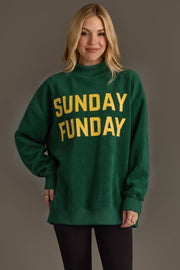 A person with blonde hair wearing the Panache Apparel Collection’s Green Game Day & Sunday Funday Reversible Sweatshirt, featuring bold yellow lettering, stands against a plain gray background, smiling gently.