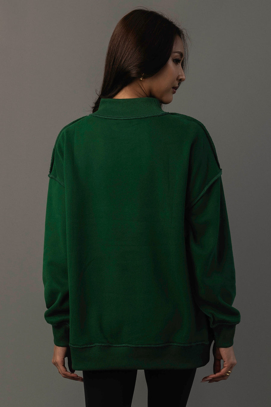 A person with long dark hair, wearing the Panache Apparel Collection Green Game Day & Sunday Funday Reversible Sweatshirt and black pants, stands facing away from the camera against a plain gray background.