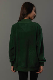 A woman with long dark hair, wearing the Panache Apparel Collection’s Green Game Day & Sunday Funday Reversible Sweatshirt and black pants, stands facing away from the camera against a plain gray background.