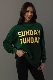A woman with long dark hair models the Panache Apparel Collection Green Game Day & Sunday Funday Reversible Sweatshirt, featuring bold yellow “SUNDAY FUNDAY” text, as she poses with one hand on her hip against a plain gray background.