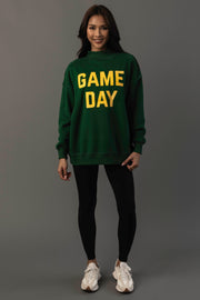 A woman stands smiling against a plain gray background, wearing the Panache Apparel Collection Green Game Day & Sunday Funday Reversible Sweatshirt, paired with black leggings and white sneakers.