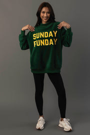 A woman smiles while wearing the Panache Apparel Collection Green Game Day & Sunday Funday Reversible Sweatshirt, styled with black leggings and white sneakers, standing against a plain gray background.