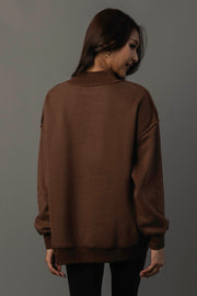 A woman with long brown hair, standing with her back to the camera and turning her head to the side against a neutral gray background, models the Panache Apparel Collection’s Brown Whiskey Weather & Bourbon Weather Reversible Sweatshirt.
