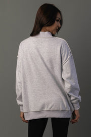 A person with long brown hair, wearing the Light Gray Whiskey Weather & Bourbon Weather Reversible Sweatshirt from Panache Apparel Collection and black pants, stands facing away from the camera against a plain gray background.