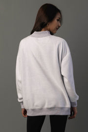 A woman with long brown hair stands facing away, wearing the Panache Apparel Collection’s Light Gray Whiskey Weather & Bourbon Weather Reversible Sweatshirt with black pants against a plain gray background.