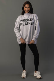 A woman stands against a plain background, smiling, wearing the Panache Apparel Collection Light Gray Whiskey Weather & Bourbon Weather Reversible Sweatshirt, paired with black leggings and white sneakers.