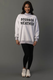 A smiling person wears the Panache Apparel Collection Light Gray Whiskey Weather & Bourbon Weather Reversible Sweatshirt, paired with black leggings and white sneakers, standing against a plain gray background.