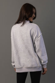 A woman with long brown hair stands with her back to the camera against a plain gray background, wearing the Panache Apparel Collection Light Gray Day Drinking & Hungover Reversible Sweatshirt and black pants.