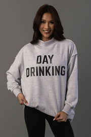 A woman smiles while wearing the Panache Apparel Collection’s Light Gray Day Drinking & Hungover Reversible Sweatshirt, featuring bold black DAY DRINKING lettering, and stands against a plain gray background.