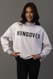 A woman smiles and stands against a gray background, wearing the Panache Apparel Collection Light Gray Day Drinking & Hungover Reversible Sweatshirt paired with black pants.