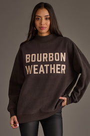 A woman is pictured wearing the Panache Apparel Collection’s Dark Gray Whiskey Weather & Bourbon Weather Reversible Sweatshirt, featuring bold lettering on the front and offering an oversized, cozy fit—ideal for embracing true Whiskey Weather style.