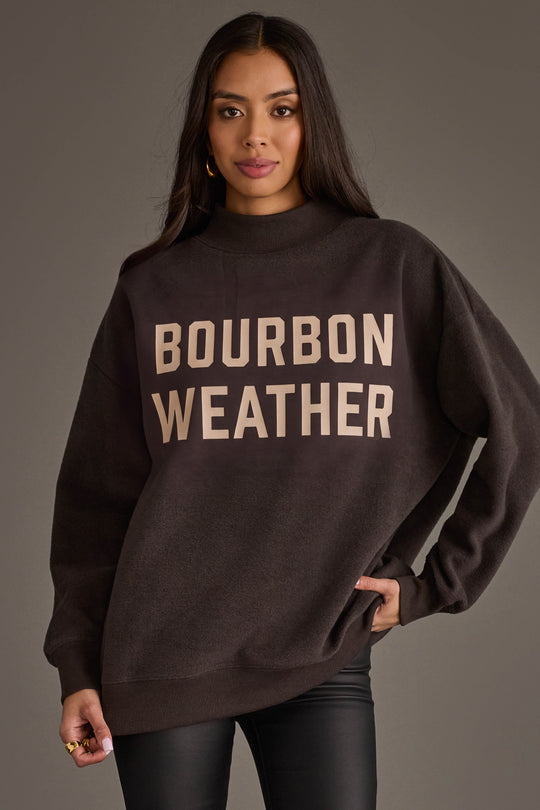 A woman is pictured wearing the Panache Apparel Collection’s Dark Gray Whiskey Weather & Bourbon Weather Reversible Sweatshirt, featuring bold lettering on the front and offering an oversized, cozy fit—ideal for embracing true Whiskey Weather style.