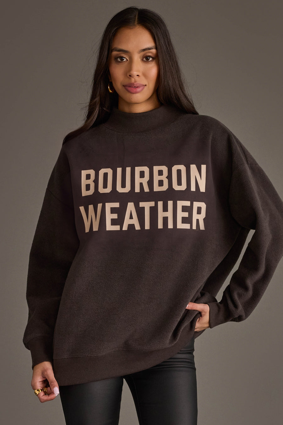 A woman is pictured wearing the Panache Apparel Collection’s Dark Gray Whiskey Weather & Bourbon Weather Reversible Sweatshirt, featuring bold lettering on the front and offering an oversized, cozy fit—ideal for embracing true Whiskey Weather style.