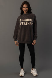 A woman stands smiling, wearing a Panache Apparel Collection Dark Gray Whiskey Weather & Bourbon Weather Reversible Sweatshirt, paired with black leggings and white sneakers, posing against a plain gray background.