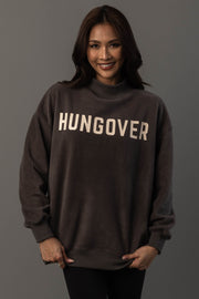 A woman smiles at the camera while wearing the Panache Apparel Collection’s Dark Gray Day Drinking & Hungover Reversible Sweatshirt. She stands against a plain, gray background.