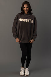 A woman stands against a gray background, smiling and wearing the Panache Apparel Collection Dark Gray Day Drinking & Hungover Reversible Sweatshirt, paired with black leggings and white sneakers.
