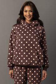 A woman stands smiling, wearing the Panache Apparel Collection Brown & Light Pink Polka Dot Hooded Sweatshirt, paired with matching pants, and poses against a plain gray background.
