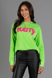 A woman wears a bright green Bright Green Merry Sweatshirt featuring the word merry in large, pink fuzzy script across the chest.