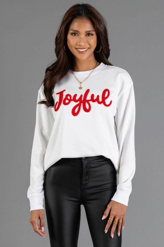 A woman wearing a white Panache Apparel Collection White Joyful Sweatshirt with the word Joyful in red script lettering across the chest.