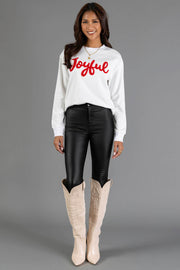 A woman wears a white Joyful Sweatshirt by Panache Apparel Collection with a crew neckline, paired with black pants and tall beige boots.