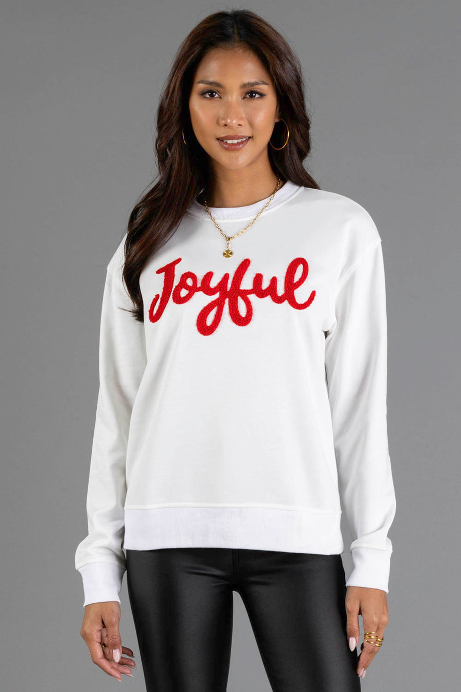 A woman wearing a white Joyful Sweatshirt with the word Joyful embroidered in red script across the chest.
