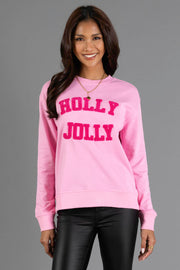 A woman wearing a pink Holly Jolly Sweatshirt with textured lettering on the chest.