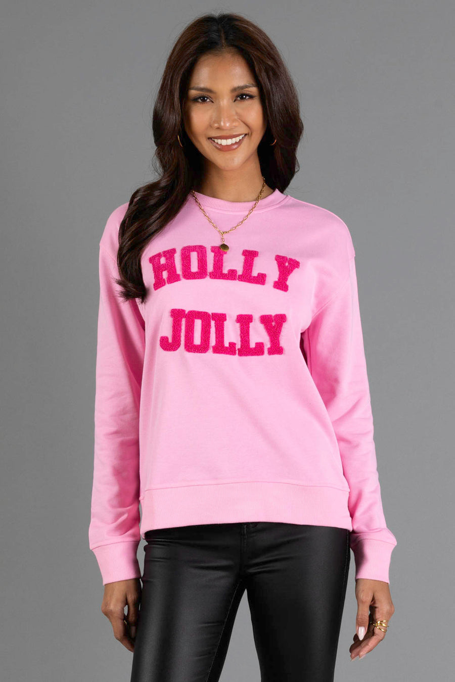 A woman wearing a pink Holly Jolly Sweatshirt with textured lettering on the chest.