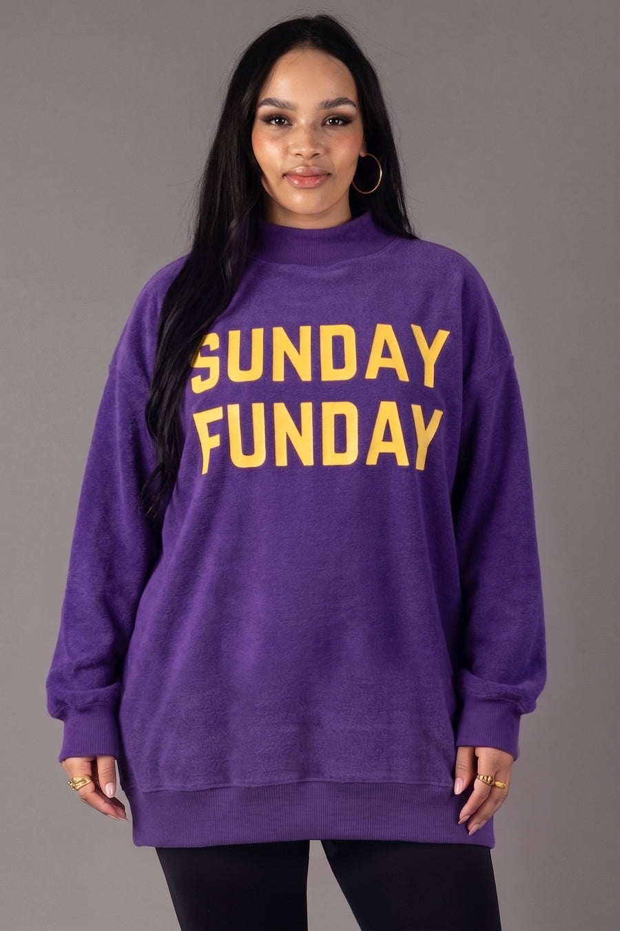 A woman stands against a gray background wearing the Panache Apparel Collection Purple Game Day & Sunday Funday Reversible Sweatshirt, featuring bold yellow lettering.