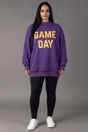 A woman stands against a gray background wearing the Panache Apparel Collection’s Purple Game Day & Sunday Funday Reversible Sweatshirt in bold yellow letters, paired with black leggings and white sneakers—creating that quintessential Sunday Funday vibe.