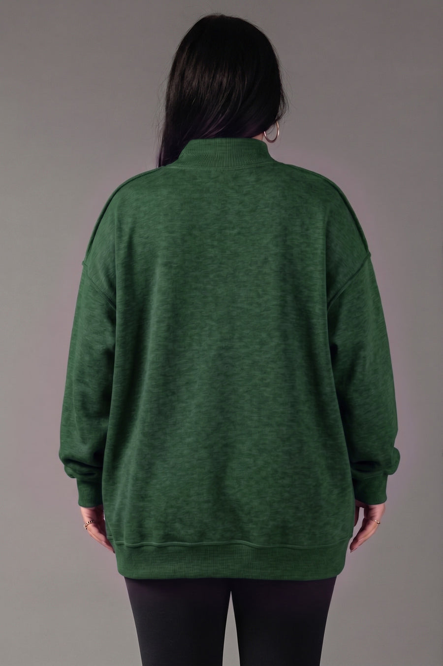 A person with long dark hair, shown from the back, wears a loose-fitting Panache Apparel Collection Green Game Day & Sunday Funday Reversible Sweatshirt and black leggings, standing against a plain gray background.
