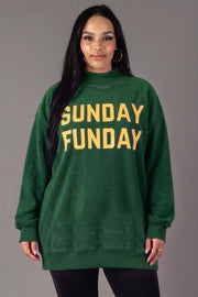 A woman with long dark hair wears the Panache Apparel Collection Green Game Day & Sunday Funday Reversible Sweatshirt, featuring bold yellow lettering, while standing against a plain gray background.