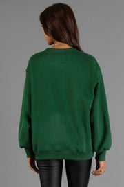 A woman with long brown hair, wearing the Panache Apparel Collection Green & Cream On Mountain Time Sweatshirt and black leather pants, is standing with her back to the camera against a plain gray background.