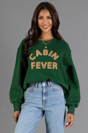 A woman wears the Panache Apparel Collection Green & Tan Cabin Fever Sweatshirt—an oversized crewneck featuring tan chenille lettering—paired with light wash jeans and a gold necklace.