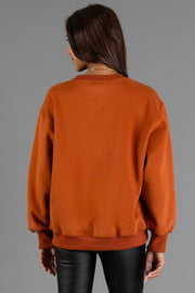 A person with long brown hair is seen from behind wearing Panache Apparel Collection’s Rust & Cream Cabin Fever Sweatshirt and black pants, standing against a plain gray background.
