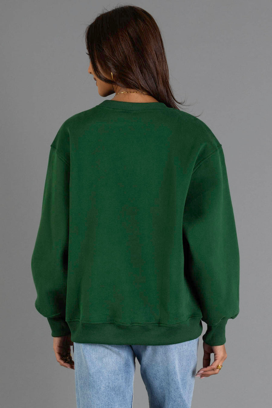 Wearing the Panache Apparel Collection’s Green & Tan Midwest Sweatshirt and light blue jeans, a person stands with their back to the camera against a plain gray background.