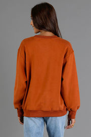 A person is seen from behind, standing against a plain gray background, wearing the Panache Apparel Collection Rust & Cream Midwest Sweatshirt paired with light blue jeans.