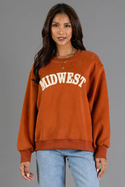 A woman wearing the Panache Apparel Collection Rust & Cream Midwest Sweatshirt, styled with light blue jeans, hoop earrings, and layered necklaces, stands against a gray background.