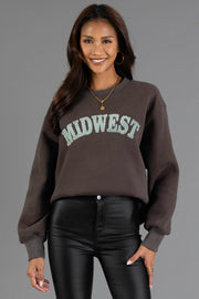 A smiling woman with long brown hair wears the Panache Apparel Collection Charcoal & Mint Midwest Sweatshirt and shiny black pants, standing against a plain gray background.