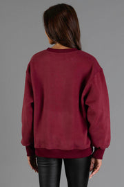 A person with long dark hair, wearing the Maroon & Cream Midwest Sweatshirt by Panache Apparel Collection and black leather pants, stands facing away against a plain gray background.