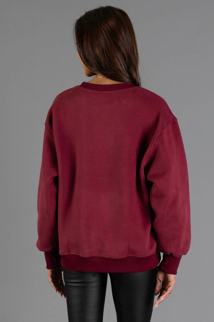A person with long dark hair, wearing the Maroon & Cream Midwest Sweatshirt by Panache Apparel Collection and black leather pants, stands facing away against a plain gray background.