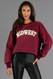 A woman with long brown hair wears the Panache Apparel Collection’s Maroon & Cream Midwest Sweatshirt paired with black leather pants, standing against a plain gray background.