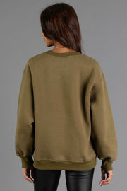 A woman with long brown hair wears the Olive & Beige Midwest Sweatshirt from Panache Apparel Collection and black leather pants, facing away from the camera against a plain gray background.